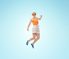 Fototapeta na wymiar summer, fashion and people concept - happy teenage girl in sunglasses jumping over blue background