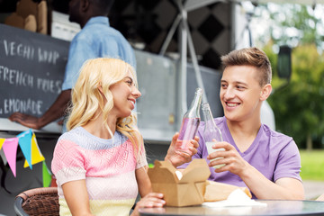 leisure, celebration and people concept - happy friends clinking bottles of non-alcoholic drinks and eating wok at food truck
