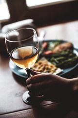 Female hand with glass of wine and food in the background