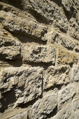 A rustic stone wall bathed in the sunshine, in colour of dried, yellow clay.