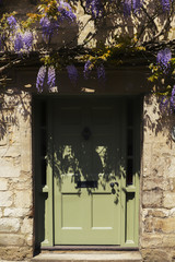 Fototapeta na wymiar Green English countryside door set in stone wall, bathed in sunshine with flowers hanging above