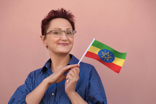 Ethiopia flag. Woman holding Ethiopian flag. Nice portrait of middle aged lady 40 50 years old with a national flag over pink wall background outdoors.