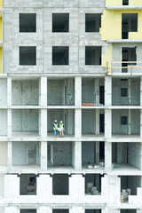 Wide angle view at two builders standing in unfinished apartment building on construction site, copy space