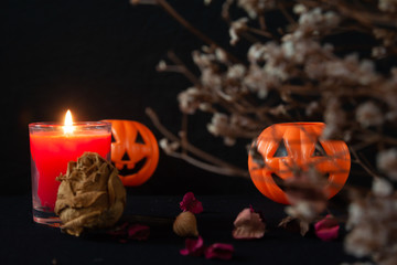 Orange pumpkin as a head with carved eyes and a smile with burning candles on a black background, Halloween home decoration