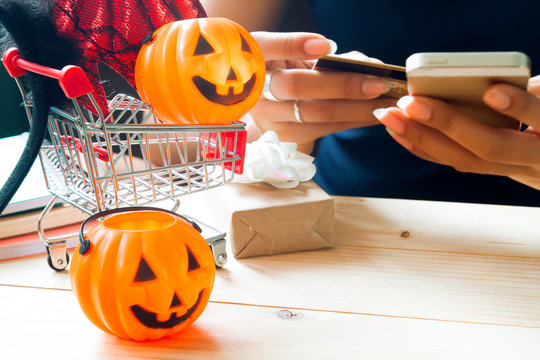 Halloween accessories and costume on shopping cart with woman using mobile phone and credit card, Happy Halloween