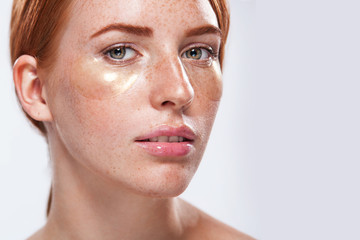 Fototapeta premium Beautiful model woman with ginger hair and frackles and gold patches for skin care