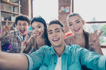 Close up portrait of cheerful youngsters make selfie on front camera of smartphone and show v-sign stand in casual wear