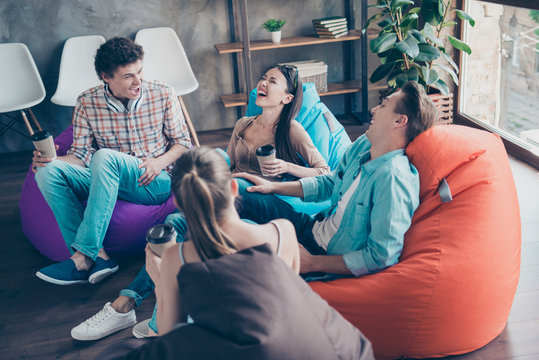 Rejoice and cheerful trandy youths sitting in a loft style room with coffee in hands tell funny stories and humorous joke to each other and aloud laugh without restraint with big toothy smile