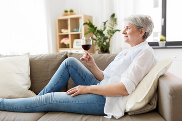 people, alcohol and leisure concept - senior woman with glass of red wine at home