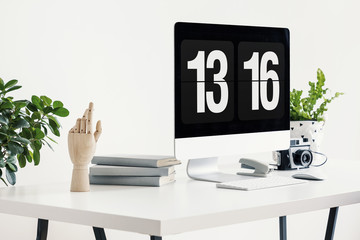 Close-up on white desk with desktop computer, camera and plants in workspace interior. Real photo
