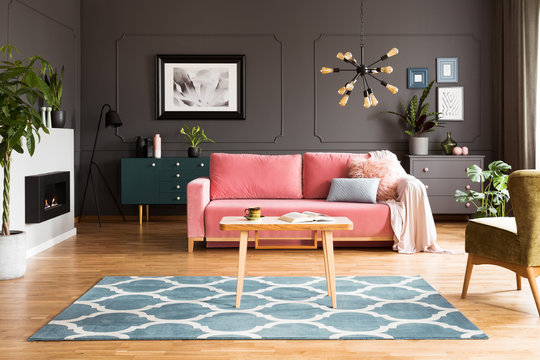 Wooden Table On Blue Carpet In Grey Living Room Interior With Fireplace And Pink Sofa. Real Photo