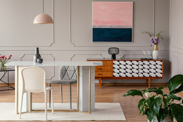White chair and marble table under pink lamp in eclectic living room interior with painting above cabinet. Real photo - obrazy, fototapety, plakaty