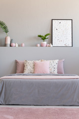 Pink carpet in front of grey bed with cushions in bedroom interior with plants and poster. Real photo