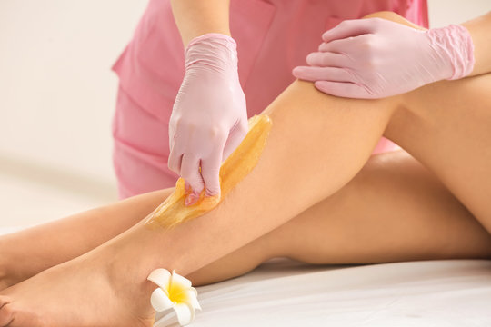 Woman having hair removal procedure on leg with sugaring paste in salon