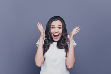 Attractive pretty nice adorable cheerful stylish brunette curly-haired girl showing stunning amazement facial expression and hands gesture, opened mouth, isolated over grey background