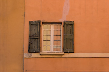 Obraz premium Old window with wooden shutters, sun blinds on bright orange color wall