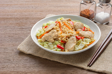 close up of stir fried instant noodle with chicken and vegetable in a ceramic dish on wooden table. asian homemade style food concept.