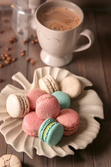 Plate with tasty macarons and coffee set on table