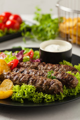 Traditional cevapcici served with baked potatoes. Stone background.