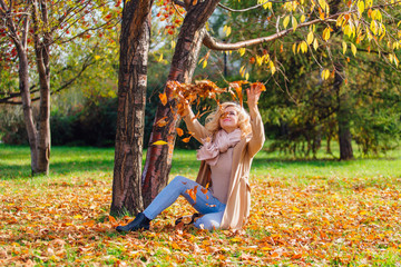 Young beautiful woman throwing up fallen autumn leaves over her head