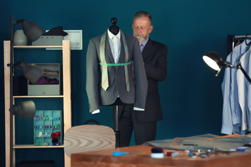 Mature tailor taking measurements of jacket on mannequin in atelier
