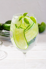 Refreshing water with slices of cucumber and basil leaves in a glass and cucumbers in a basket