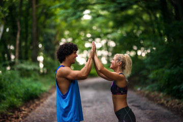 Fit young strong couple giving high five to each other. Standing on running track in a park.