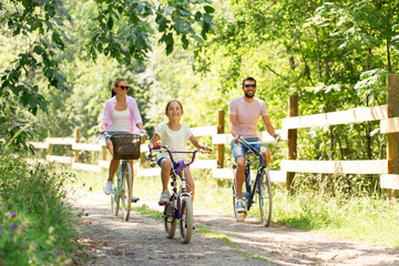 family, leisure and people concept - happy mother, father and little daughter riding bicycles in summer park