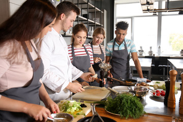 Chef and group of young people during cooking classes - obrazy, fototapety, plakaty