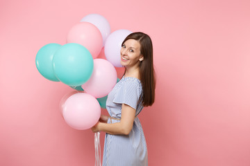 Fototapeta na wymiar Portrait of attractive smiling young happy woman wearing blue dress holding colorful air balloons isolated on bright trending pink background. Birthday holiday party, people sincere emotions concept.