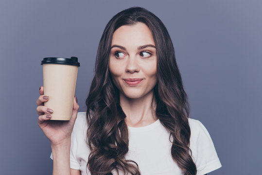 Close-up portrait of attractive pretty lovely stylish nice cute cheerful curly-haired brunette girl in casual white t-shirt, holding, looking at paper-cup coffee, isolated on grey background