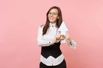 Young joyful attractive business woman in black suit, glasses holding bitcoin, up arrow isolated on pastel pink background. Lady boss. Achievement career wealth concept. Copy space for advertisement.