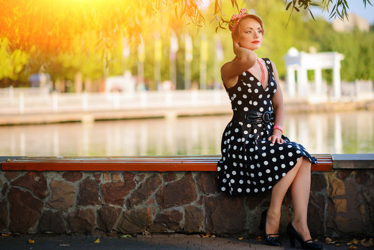 A beautiful young woman dressed sits on a bench near the pond