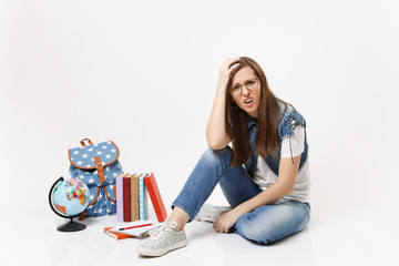 Young dissatisfied upset woman student in denim clothes clinging to head sitting near globe,...