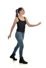  full length portrait of brunette girl wearing black single and jeans. standing pose in side profile. isolated on white studio background.