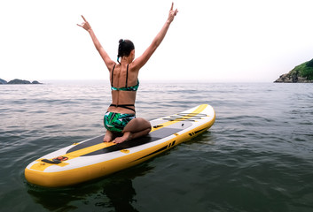 Vacations at sea: the girl sails on a yellow sup-board and on sea waves and happily lifts her hands to the top.