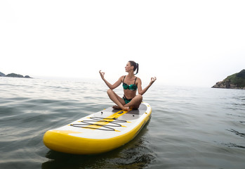 Fototapeta na wymiar Vacation at sea: the girl sails on a yellow sup-board and meditates in a lotus position.