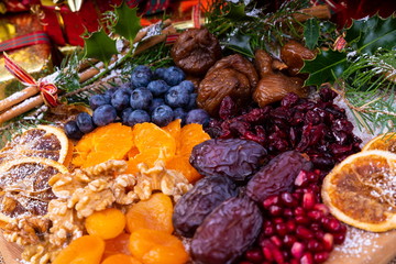 Platter of Festive Christmas Fruits.  Wooden Platter loaded with a selection of fresh and dried Christmas Fruits.  Decorated with Holly, Cinnamon and Christmas parcels.