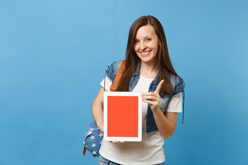 Obraz premium Young joyful pretty woman student pointing index finger up holding tablet pc computer with blank black empty screen isolated on blue background. Education in university. Copy space for advertisement.