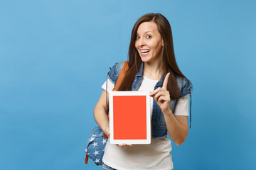 Obraz premium Young funny cheerful woman student pointing index finger up, holding tablet pc computer with blank black empty screen isolated on blue background. Education in college. Copy space for advertisement.