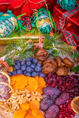 Platter of Festive Christmas Fruits.  Wooden Platter loaded with a selection of fresh and dried Christmas Fruits.  Decorated with Holly, Cinnamon and Christmas parcels.