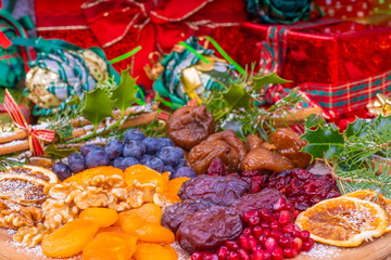 Platter of Festive Christmas Fruits.  Wooden Platter loaded with a selection of fresh and dried Christmas Fruits.  Decorated with Holly, Cinnamon and Christmas parcels.
