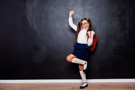 Full size body length of glad smart cute stylish small little girl with curly ponytails in white blouse shirt and blue skirt with red bag, celebrating. Isolated over black background