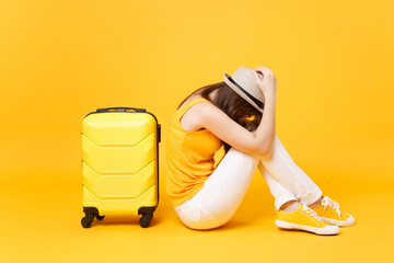 Sad traveler tourist woman in summer casual clothes, hat sit near suitcase isolated on yellow...