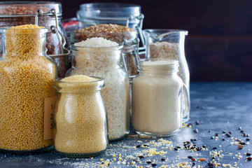 Various cereals in glass jars - rice, millet, oatmeal, couscous, buckwheat, semolina, copy space