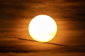 Extreme close up of the sun setting with dramatic red clouds at sunset. Plane trail. High Definition - Shot with pro zoom lens