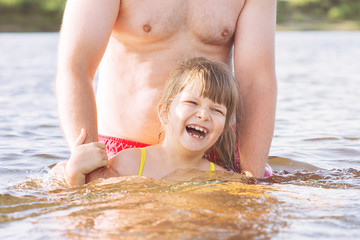 A young bearded father with glasses with a small blond daughter splashing in the river in sunny summer weather