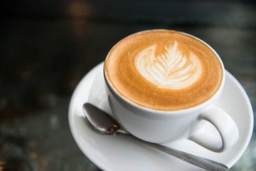 White cup of coffee latte art leave from fresh milk on the table.