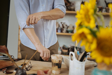 Work table. Handyman wearing striped shirt and brown trousers standing near his wooden work table