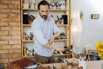 New workshop. Bearded dark-haired handicraftsman in striped shirt and brown trousers standing in his new workshop